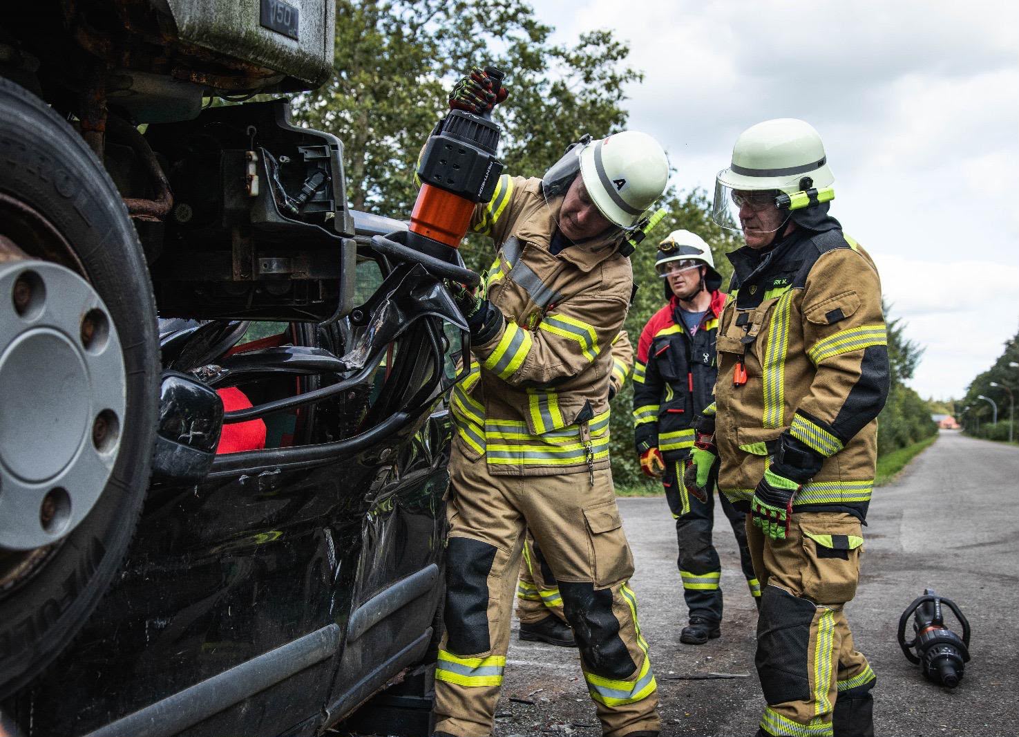 Feuerwehrleute in Einsatzmontur arbeiten mit hydraulischen Rettungsgeräten an einem verunglückten Lastwagen.